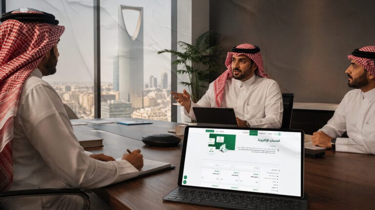 صورة-الغلاف-اجتماع-أعمال-احترافي-في-الرياض-يظهر-به-رجال-اعمال،-يظهر-فيه-جهاز-و-به-واجهة-منصة-اعتماد-وشعار-فطين-بشكل-مبسط